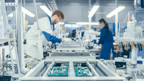 Shot of an Electronics Factory Workers Assembling Circuit Boards by Hand While it Stands on the Assembly Line. High Tech Factory Facility. photo