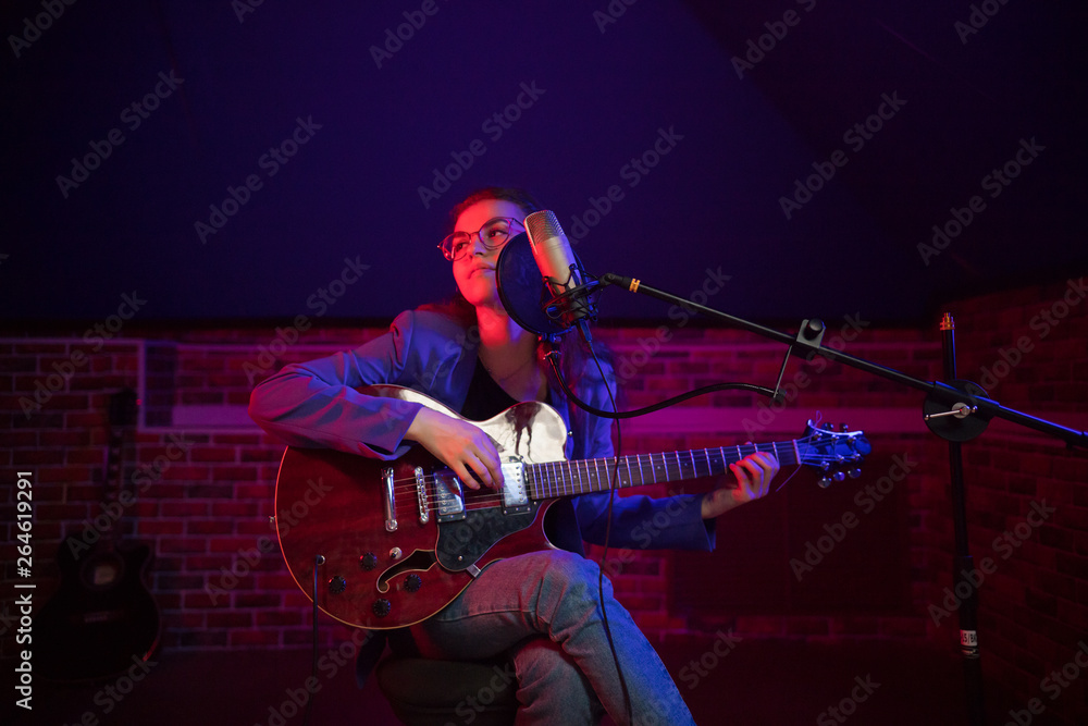 Obraz premium A young woman in glasses playing guitar and singing in neon lighting