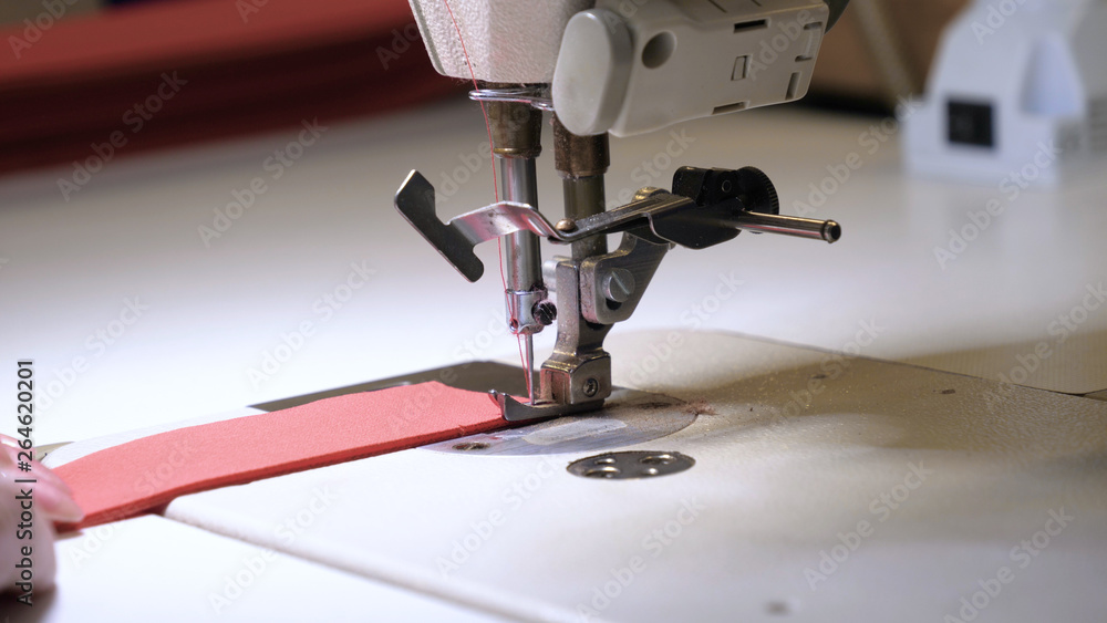 Fototapeta premium A seamstress in a seamstress factory (at home) sews clothes from fabric materials. Using a sewing machine in slow motion. Concept of: Factory, Work, Labor, Cloth, People, Macro, Clothes.