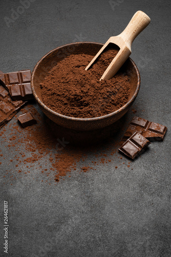 Dark Chocolate chunks and cocoa powder in wooden scoop on dark concrete background