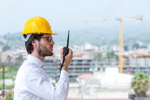 Ingegnere capo da ordini con la radio ricetrasmittente per le operazioni in cantiere con la gru e la costruzione del nuovo edificio. photo