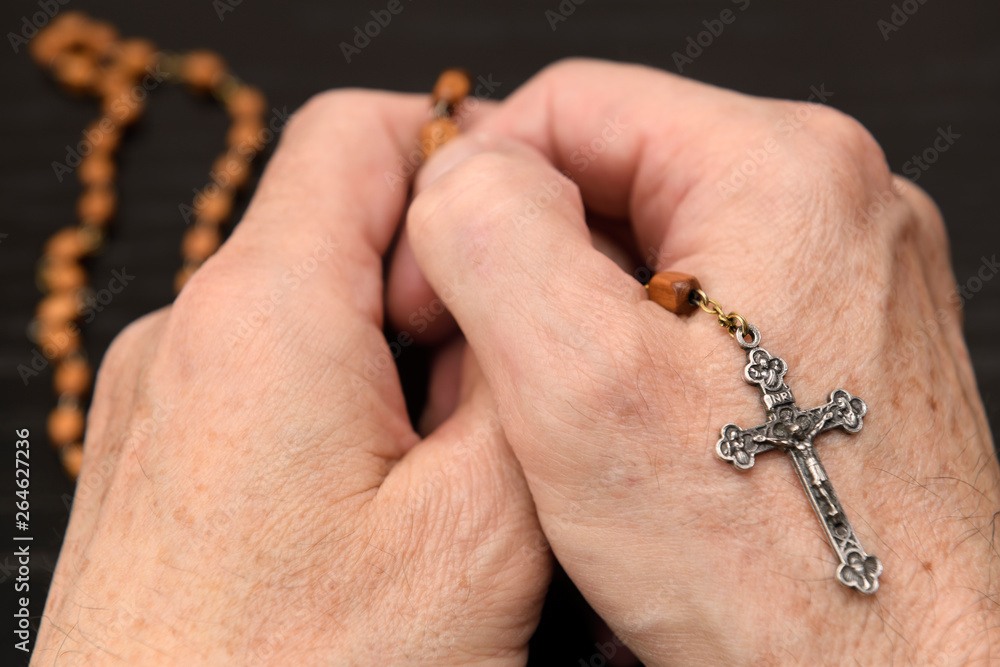 Hands of old man meditating and praying on the wood beads of a holy rosary with crucifix Hands of old man meditating and praying on the wood beads of a holy rosary with crucifix
