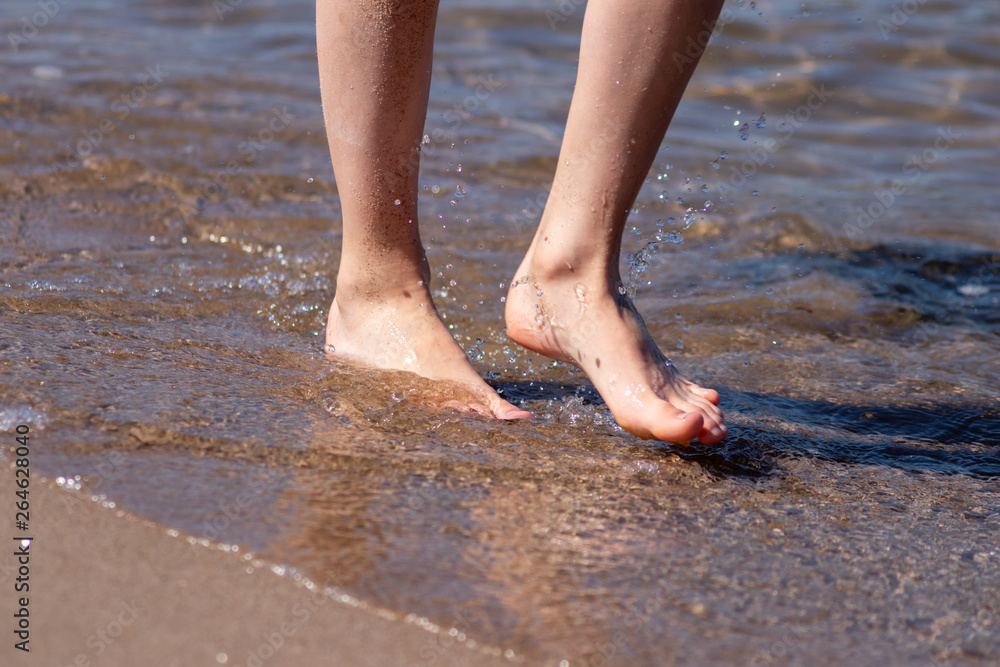 Kind läuft barfuß am Strand entlang mit platschenden Füßen im Wasser und schöner Wasserfontäne Kind läuft barfuß am Strand entlang mit platschenden Füßen im Wasser und schöner Wasserfontäne