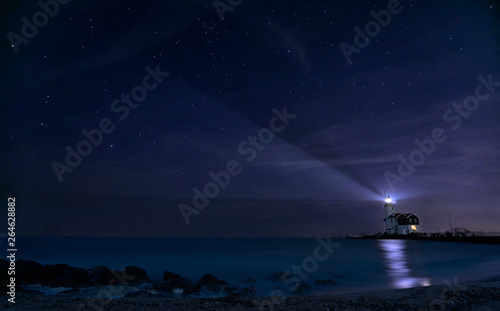 Lighthouse shining beam of light into the night sky over blue lake as a navigation beacon for ships