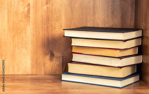 Pile of closed books on wooden shelf.