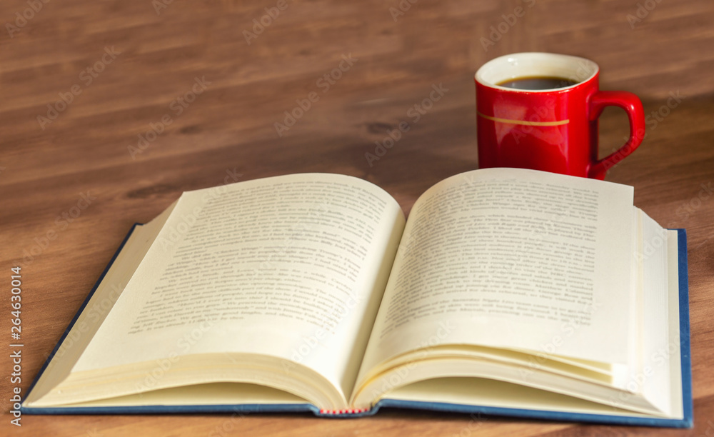 Open book with cup of coffee on wooden background.