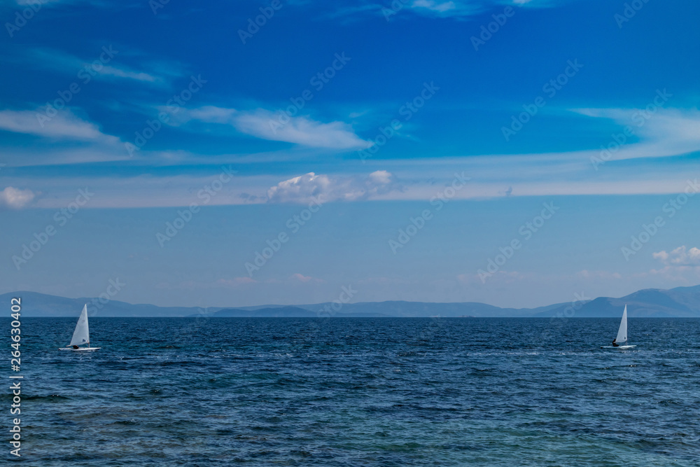 Small optimist boats with white sails, blue sky and sea background