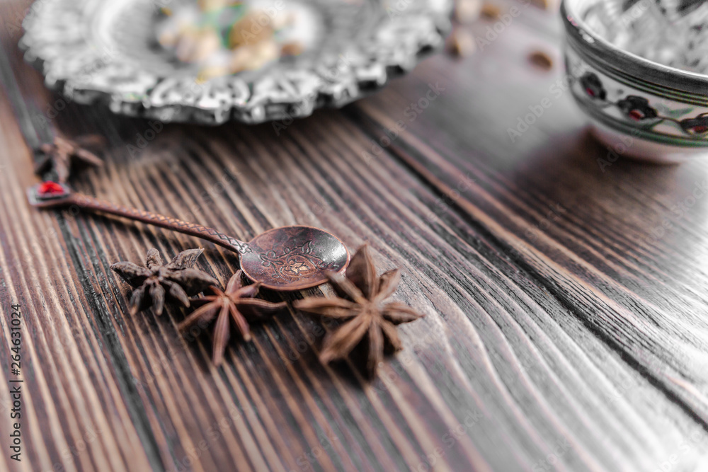 Authentic middle east style bronze spoon with a cinnamon on the wooden desk with a colourful eastern bowl and a plate on the black background. Isolated. Shallow depth of field. Horizontal orientation. Authentic middle east style bronze spoon with a cinnamon on the wooden desk with a colourful eastern bowl and a plate on the black background. Isolated. Shallow depth of field. Horizontal orientation.