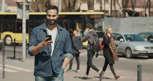 Casual dressed bearded man walking down the street while using smartphone for chat
