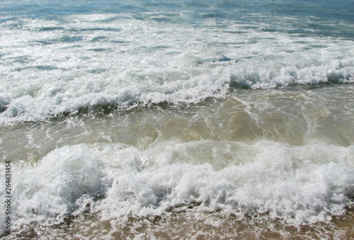 White waves crashing and splashing with foam near the shore in the sun on the ocean for the background.