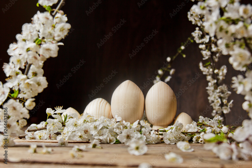 wooden easter eggs among flowering cherry branches on a rustic table. symbolic composition of the spring holiday for a gift card. copy space. close up. petals of white flowers. the rebirth of nature