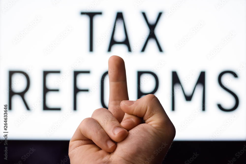 Businessman showing middle finger to a screen with inscription TAX REFORMS. Government decides to raise taxes for a business Businessman showing middle finger to a screen with inscription TAX REFORMS. Government decides to raise taxes for a business
