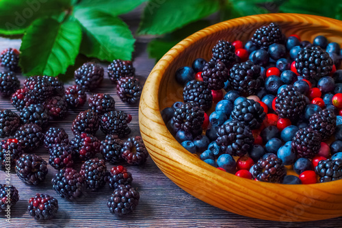 berry background. a mixture of ripe fresh berries in a wooden bowl close-up. blackberries, blueberries cranberries on the table.