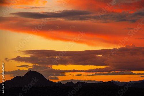 Clouds reflecting the light of a colorful sunset with a distant mountain at the bottom of the image.