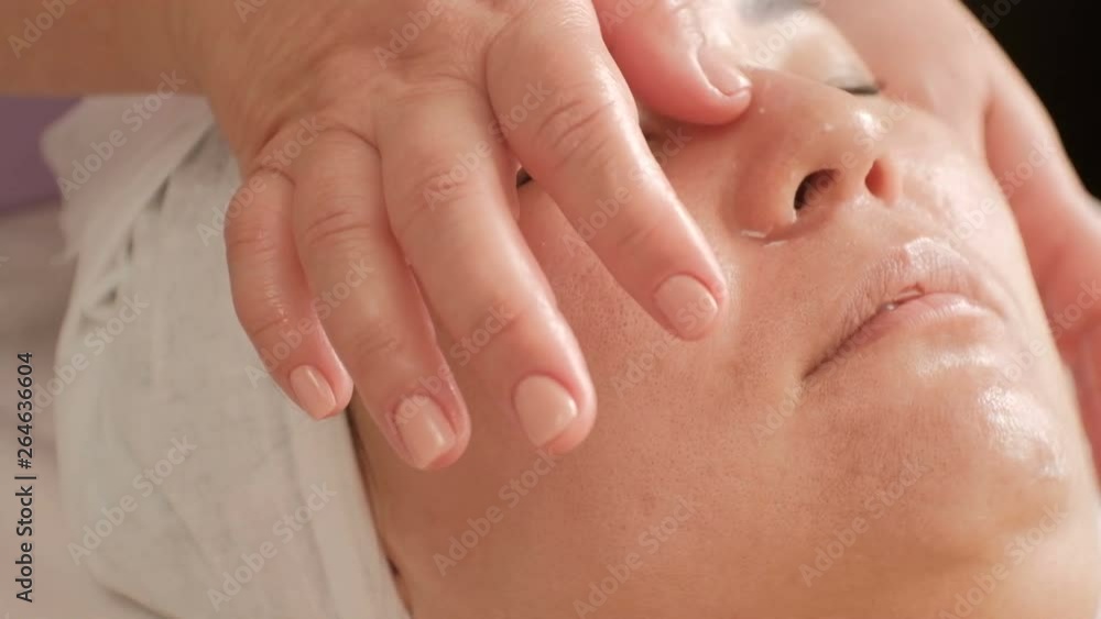 Anti-aging facial massage. Close-up. The hands of a professional cosmetologist smooth the skin on the face of an Asian girl. SPA beauty salon. Anti-aging facial massage. Close-up. The hands of a professional cosmetologist smooth the skin on the face of an Asian girl. SPA beauty salon.