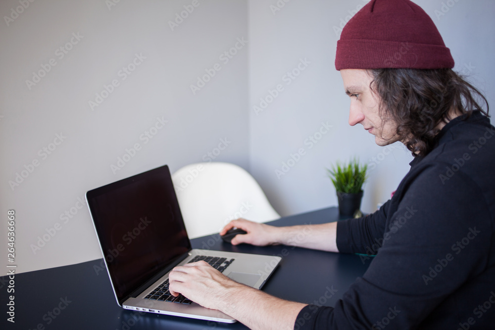 Designer for a laptop, a workplace for freelancers. A young man sitting at a table Designer for a laptop, a workplace for freelancers. A young man sitting at a table