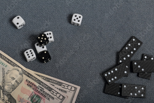 White dice with black markings. They lie on a surface covered with a coarse gray cloth. Among them are two black dice with white markings. Next door are dominoes and dollars.