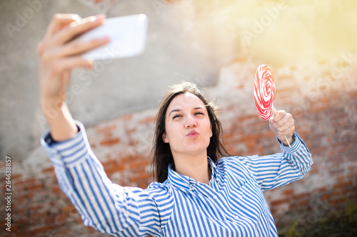 Young female with lollipop making selfie.