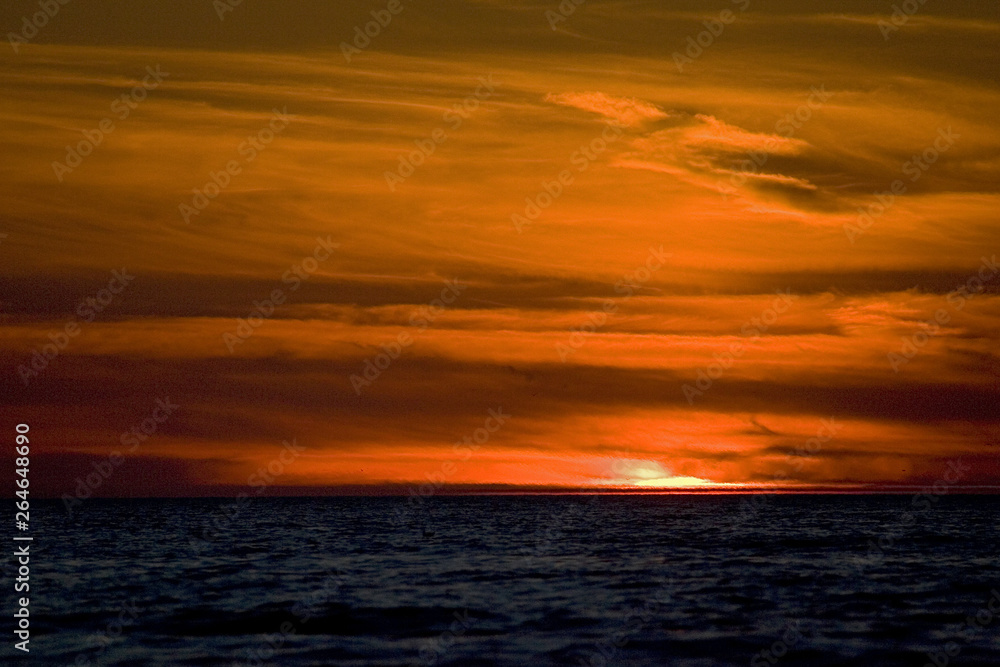 Stunning sunset on North sea at Katwijk, Netherlands. Sun going down over the horizon with dramatic red sky.