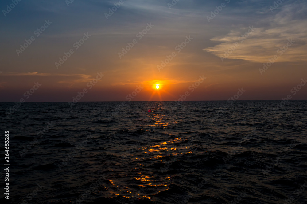 Bright sunset with large yellow sun under the sea surface. sunrise in the sea. Beautiful sunset above the sea. Tropical sunset on the beach.