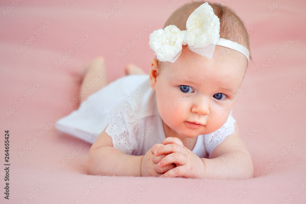 Portrait of a cute newborn baby girl in white dress and hairband lying on her stomach Portrait of a cute newborn baby girl in white dress and hairband lying on her stomach