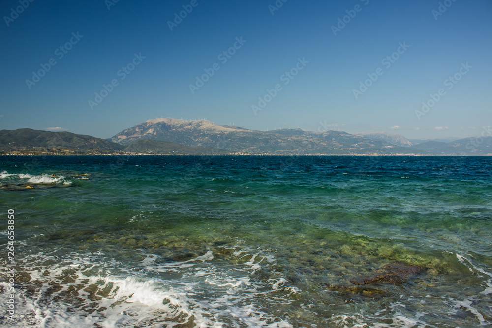 Aegean sea summer scenic landscape in Greece with waves near waterfront and mountain ridge background 