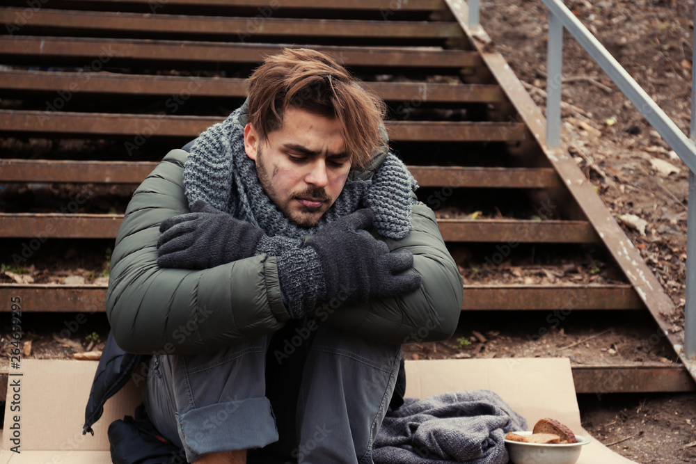 Poor young man sitting on stairs outdoors Poor young man sitting on stairs outdoors