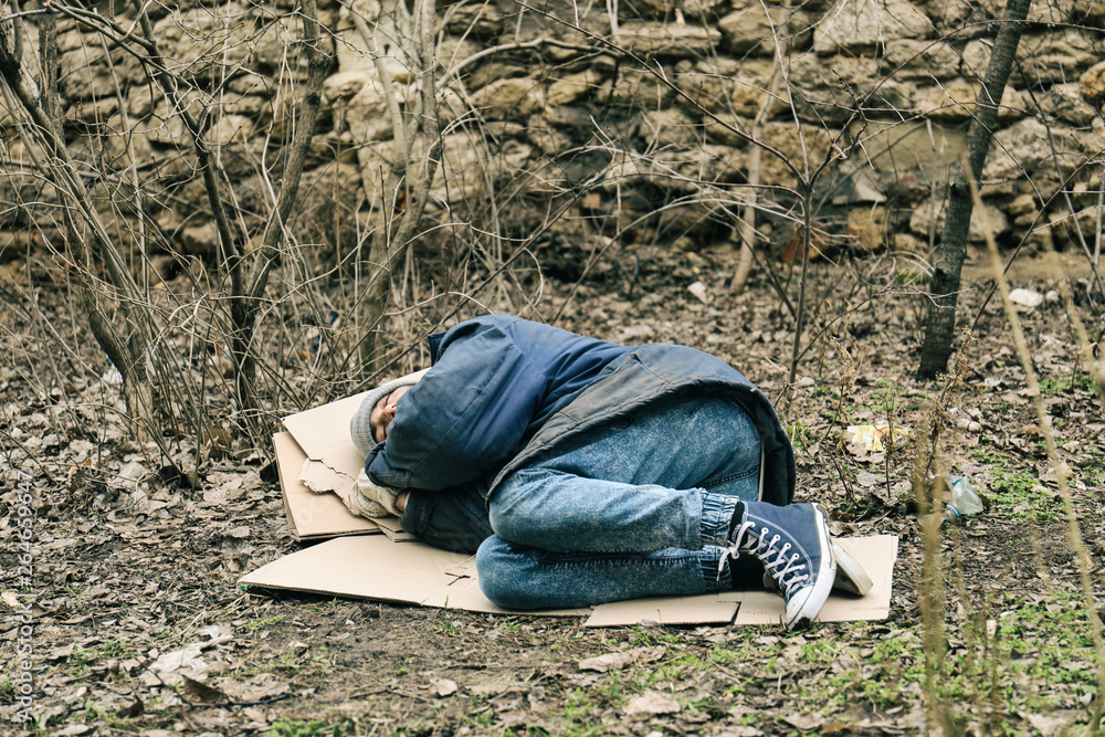 Poor homeless man lying on ground in city park Poor homeless man lying on ground in city park