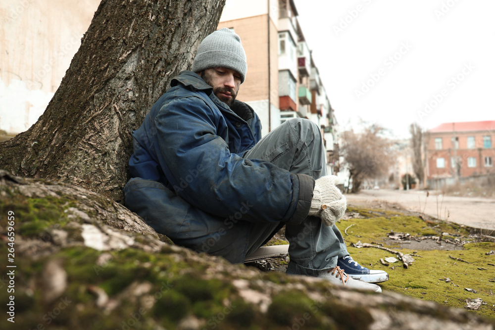 Poor homeless man sitting on ground outdoors Poor homeless man sitting on ground outdoors