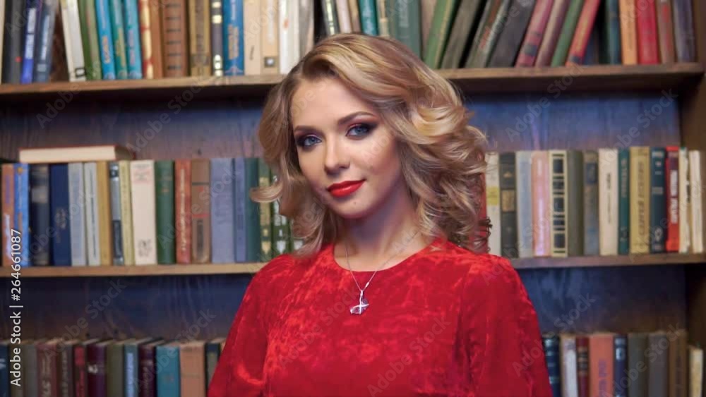 Beautiful sexy blonde with bright makeup in red dress posing in the interior with books. The beauty of the face and body. Photos shot in a studio interior Beautiful sexy blonde with bright makeup in red dress posing in the interior with books. The beauty of the face and body. Photos shot in a studio interior