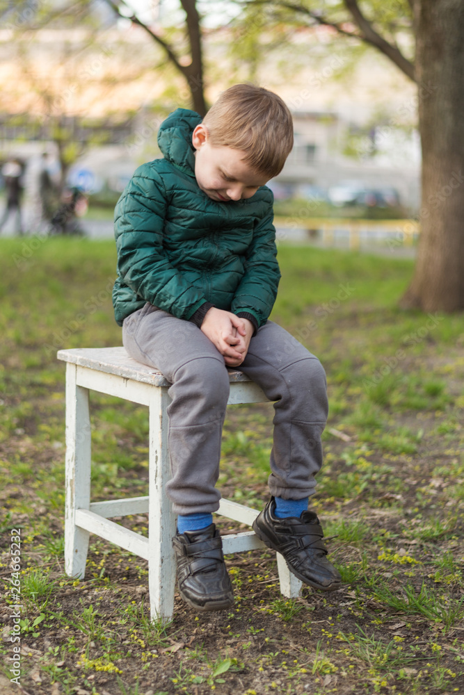 A little boy sadly sits on a stool in nature. A little boy sadly sits on a stool in nature.