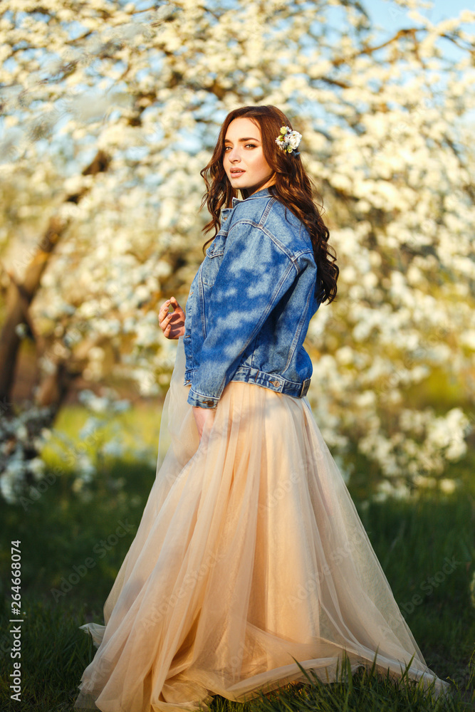 Portrait of a beautiful bride. Wedding concept. Stylish wedding. Great sunset light. She is wearing a blue denim jacket, dress. Spring blooming garden. Portrait of a beautiful bride. Wedding concept. Stylish wedding. Great sunset light. She is wearing a blue denim jacket, dress. Spring blooming garden.