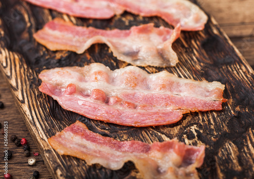 Grilled oily bacon rashers on vintage chopping board close up.