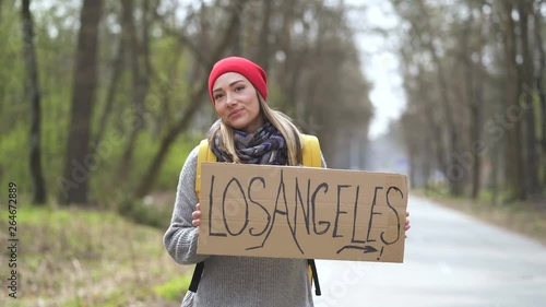 Waiting car. Young hitchhiking girl on road with poster Los Angeles.  photo