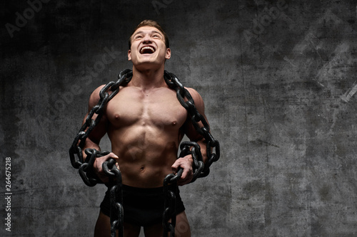 The concept of overcoming your weakness. Muscular pumped bodybuilder on black background. Sexy athlete man with huge chain around his neck