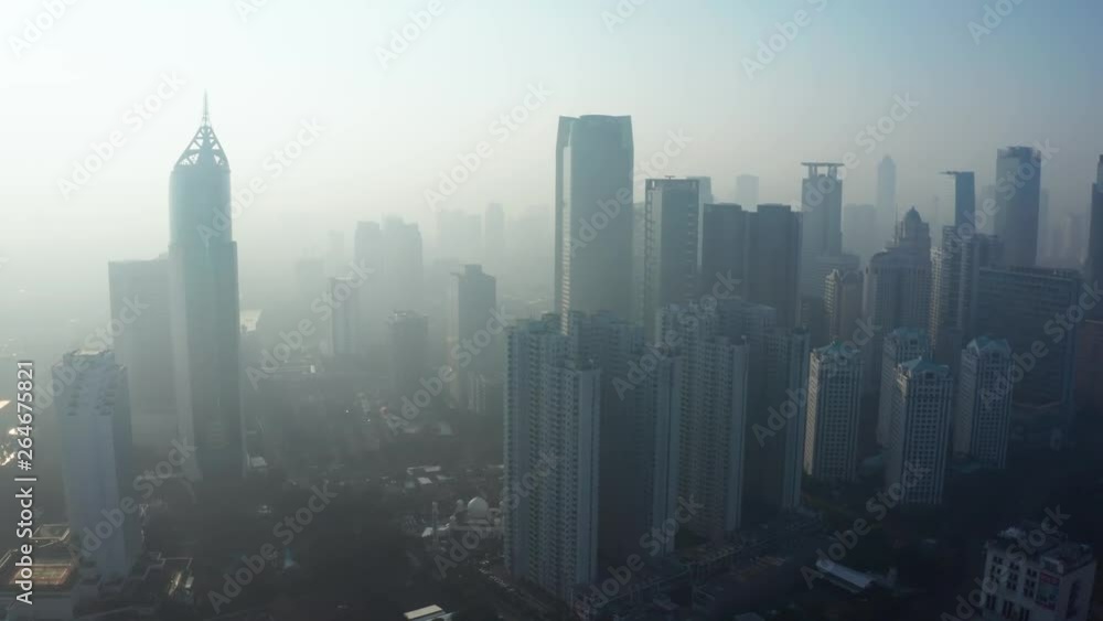 JAKARTA, Indonesia - April 25, 2019: Aerial view of Jakarta skyline with silhouette of modern skyscrapers covered by fog of air pollution. Shot in 4k resolution from a drone flying forwards JAKARTA, Indonesia - April 25, 2019: Aerial view of Jakarta skyline with silhouette of modern skyscrapers covered by fog of air pollution. Shot in 4k resolution from a drone flying forwards