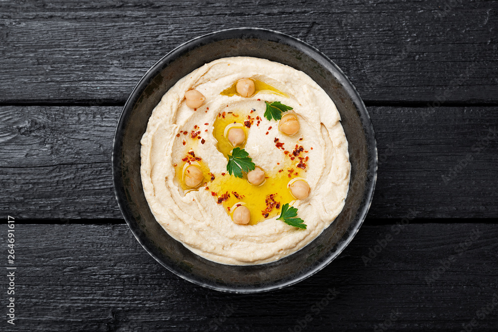 Hummus, chickpea dip, with spices in a black plate on black wooden background. Hummus, chickpea dip, with spices in a black plate on black wooden background.