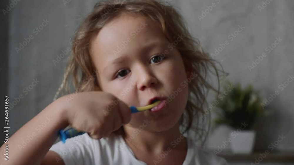 Portrait of little cute kid girl is intensively brushing her teeth with toothbrush and looking at camera in bathroom, face closeup. Portrait of little cute kid girl is intensively brushing her teeth with toothbrush and looking at camera in bathroom, face closeup.