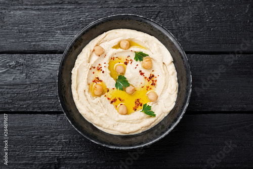 Hummus, chickpea dip, with spices in a black plate on black wooden background. 