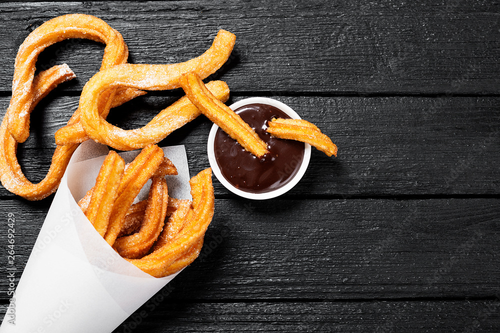 Fotografía Churros with sugar and chocolate sauce on black wooden  background | Posters.es