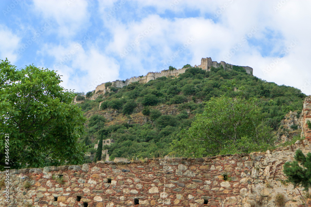 View from below to Mystras hill with ruins of medieval Villehardouin's Castle and clouds and blue sky above