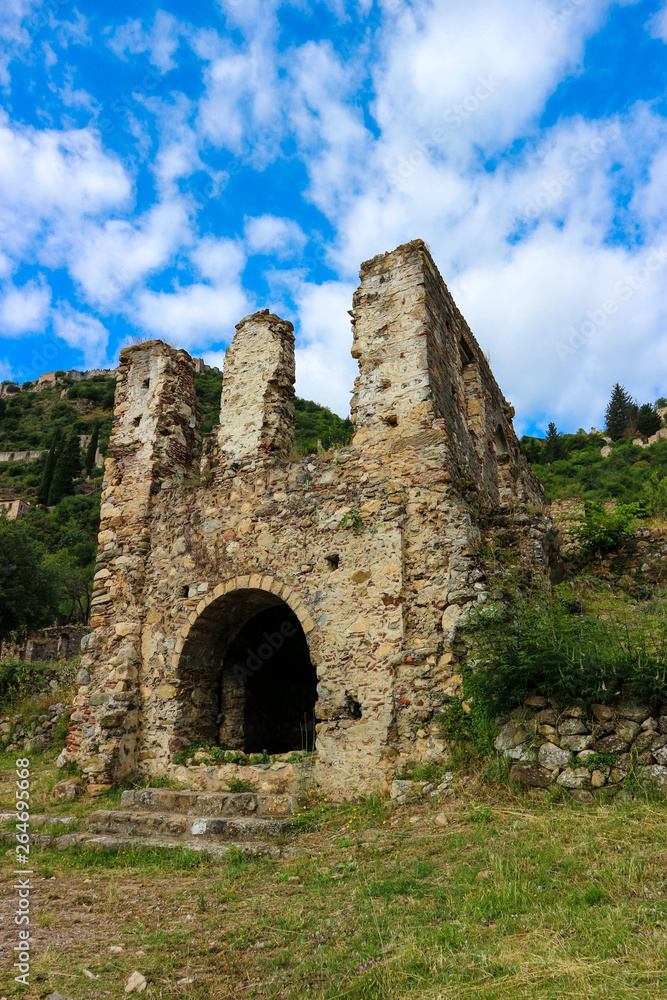Beautiful and romantic ruins of the stone medieval house with arch blue sky with clouds on the background, abandoned city Mystras, Peloponnese, Greece