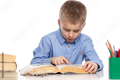 The schoolboy sits at the table and does his homework. Isolated on a white background.