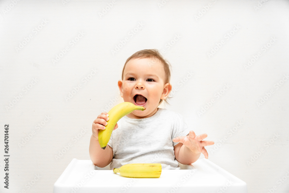 Funny little toddler eating banana in a high chair copy space food baby Funny little toddler eating banana in a high chair copy space food baby