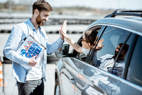 Tableau sur toile Instructor giving a five to a woman driver sitting in the car while learning to
