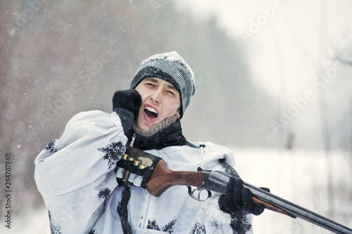 Man (hunter) in winter camouflage hit the butt of a gun in the chin from the recoil when fired
