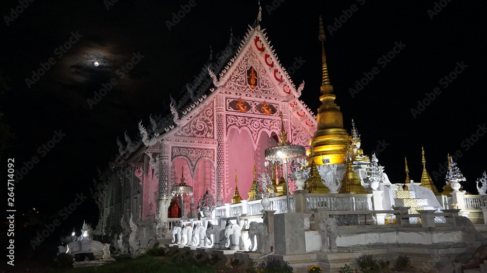 Buddhist temple is pink color at night with moon in sky
