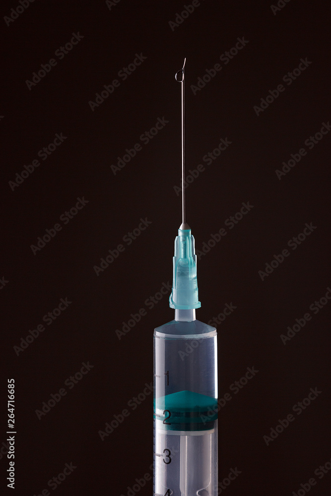 The end of the syringe with a needle filled with liquid on a dark background. The end of the syringe with a needle filled with liquid on a dark background.