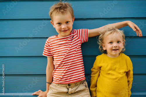 Outdoor portrait of big brother and his little sister against blue house wall