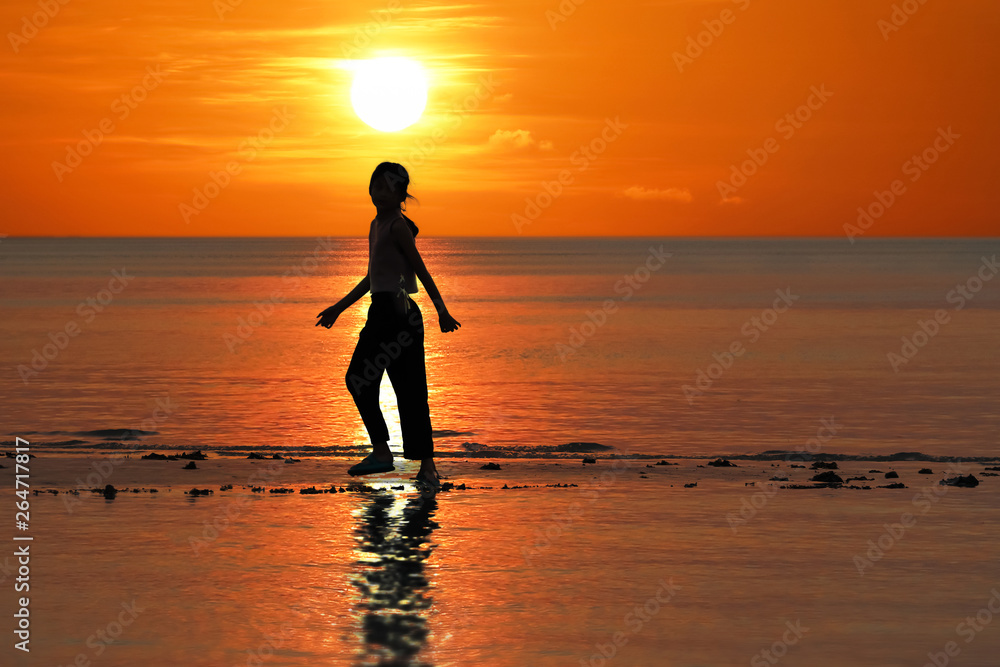 Silhouette of single Asian girl enjoying herself during sunset on the beach red sky